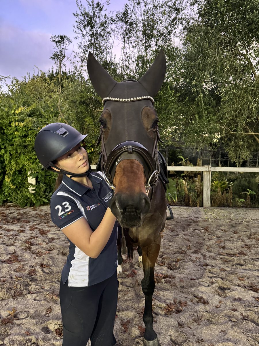 Ruby in riding gear standing with her horse in the arena